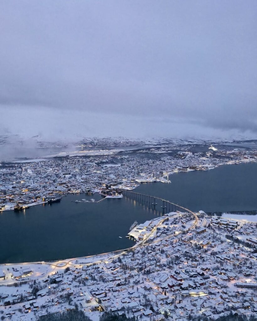 The stunning panoramic view from the Fjellheisen Cable Car in Tromsø, showing the city, fjords, and snow-covered mountains below.