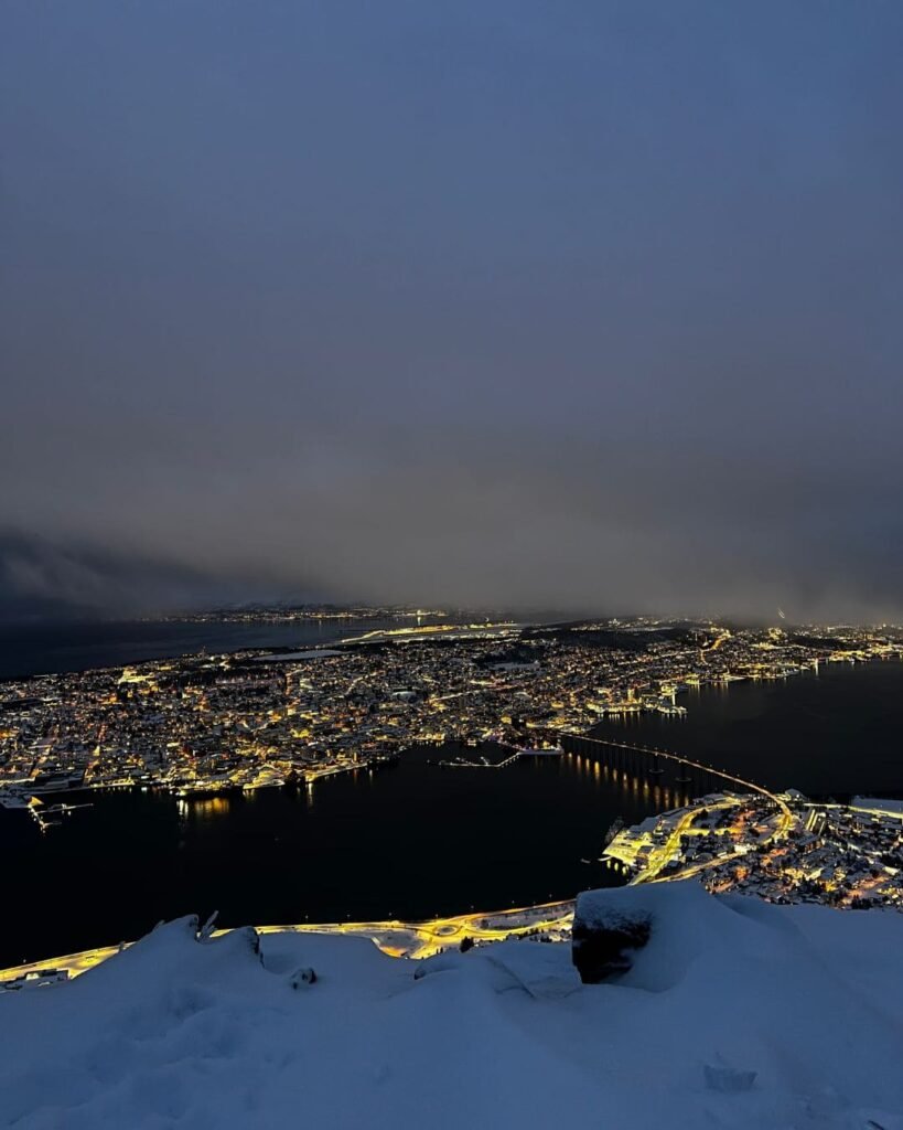 The stunning panoramic view from the Fjellheisen Cable Car in Tromsø, in the night showing the city, fjords, and snow-covered mountains below.