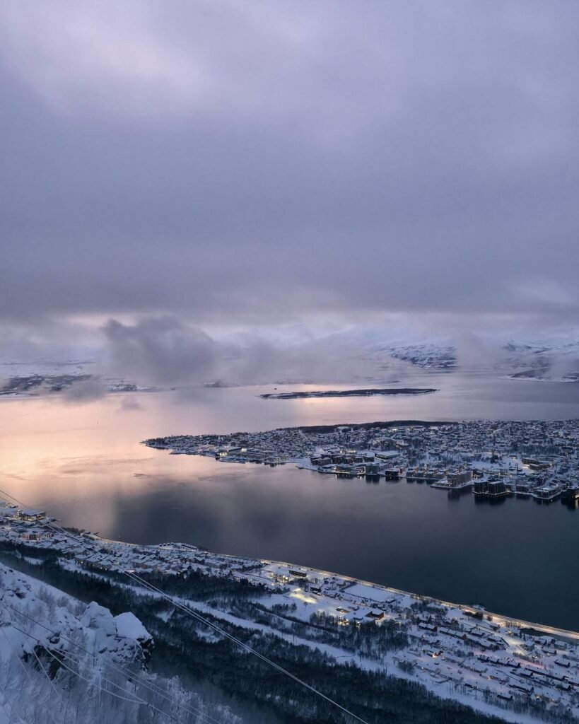 The stunning panoramic view from the Fjellheisen Cable Car in Tromsø, showing the city, fjords, and snow-covered mountains below.