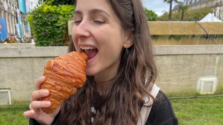 Rumi enjoying a freshly baked Parisian croissant with a golden, crispy exterior and soft, flaky layers inside.
